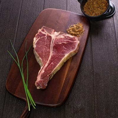 A bone in steak on a dark wooden board, with chives beside it