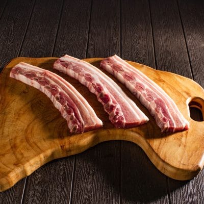 Four pork ribs lined up on a light wooden board
