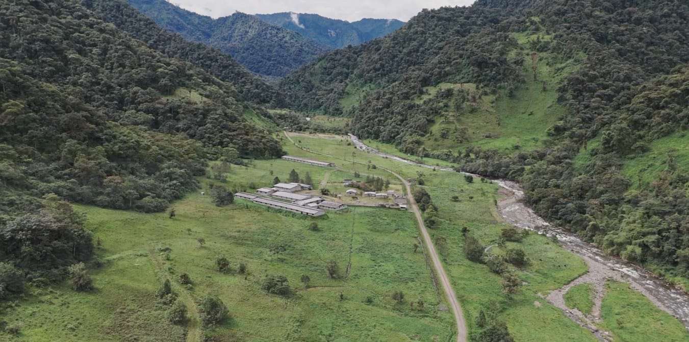 Vista aérea de una granja en un valle amazónico: naves de producción entre potreros, junto a un río y rodeadas de montañas cubiertas de bosque